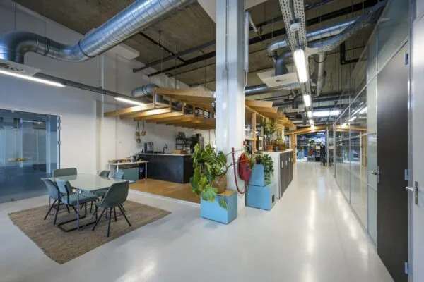 Moderne kantoorruimte aan de Joan Muyskenweg met open keuken, zithoek en industriële plafondleidingen.